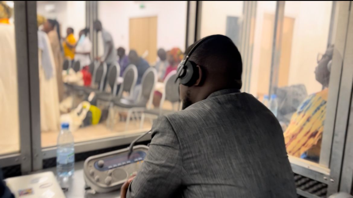 Interprète en cabine, casque sur les oreilles, face à une assemblée vue à travers la vitre